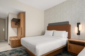 Una habitación de hotel con una cama, mesitas de noche de madera, un armario con perchero y una lámpara fijada a la pared.