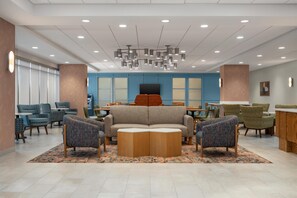 Eine moderne Lobby mit einer Couch, Sesseln, einem Couchtisch und einem Fernseher.