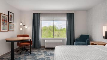 A hotel room with a bed, a desk, a chair, a window with curtains, and framed pictures on the wall.