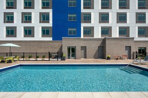 Une piscine dont le bord est recouvert de carreaux bleus, un bâtiment en briques agrémenté d’une touche de bleu, et des espaces de détente en plein air.