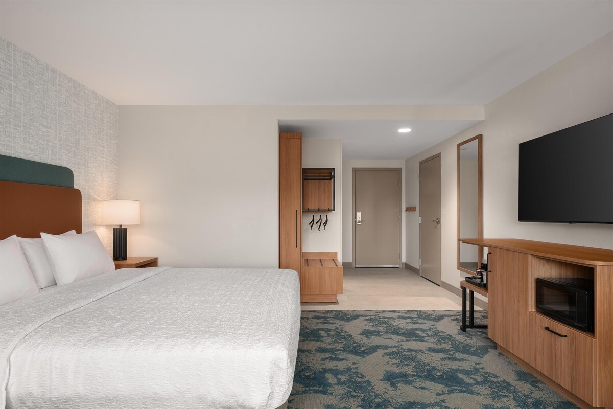 Una habitación de hotel con cama, televisión, aparador de madera y escritorio.