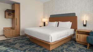 A modern hotel room with a large bed, wooden nightstands, a wardrobe, and a patterned carpet.