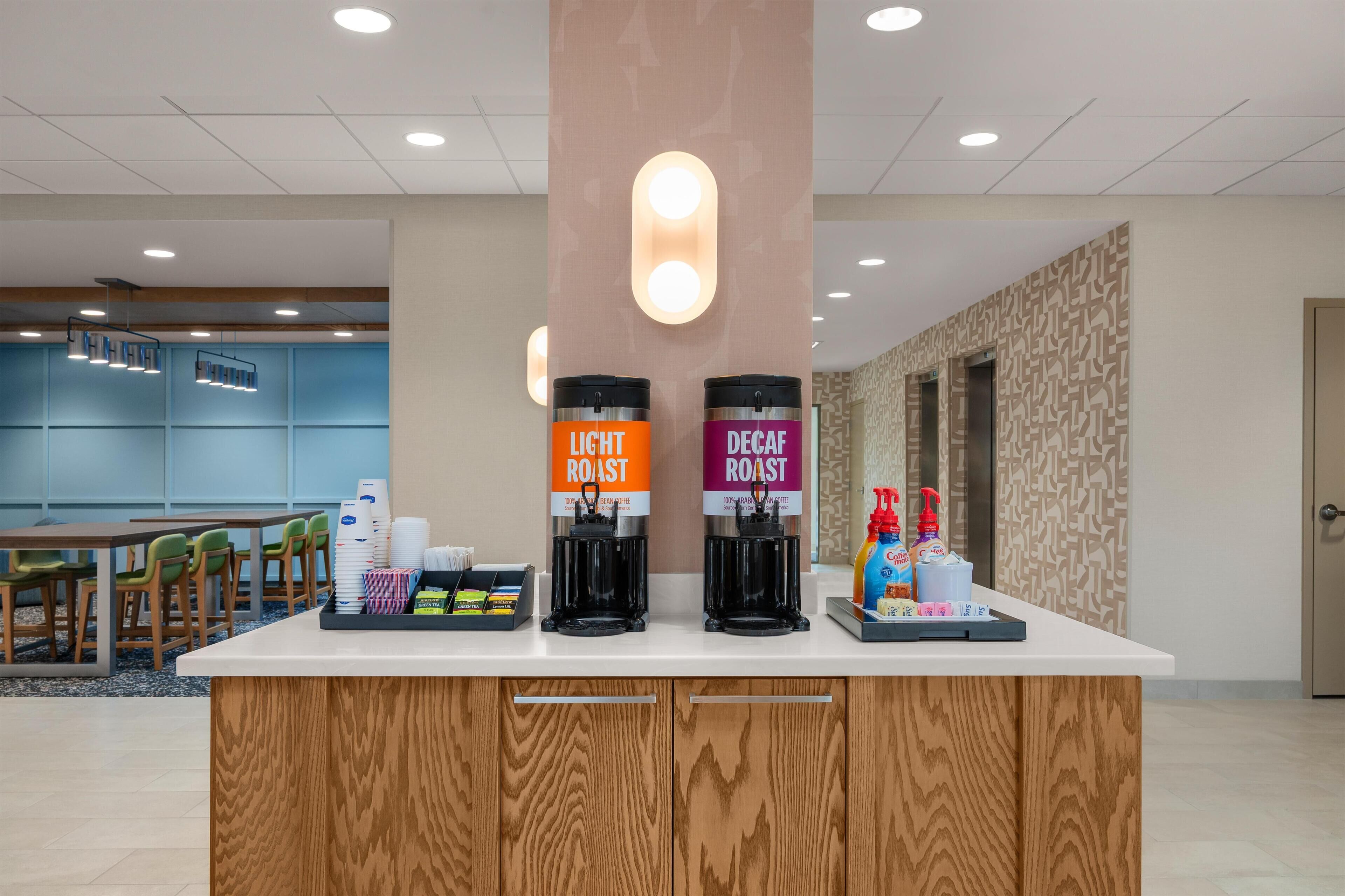 A coffee station with two coffee dispensers labeled 'Light Roast' and 'Decaf Roast' and a tray with disposable cups and condiments.