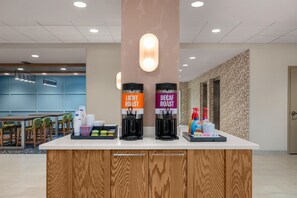A coffee station with two coffee dispensers labeled 'Light Roast' and 'Decaf Roast' and a tray with disposable cups and condiments.