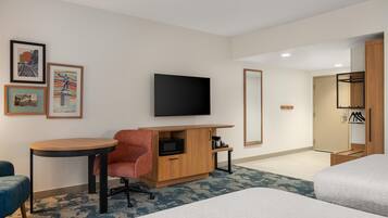 A hotel room with a bed, a desk with a chair, a television, a wardrobe, and framed pictures on the wall.