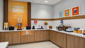 A kitchen area with a large sign for The Hampton Waffle, a coffee station, and various food items on the counter.