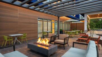 An outdoor patio with a fire feature, seating, and a covered area with tables and chairs.