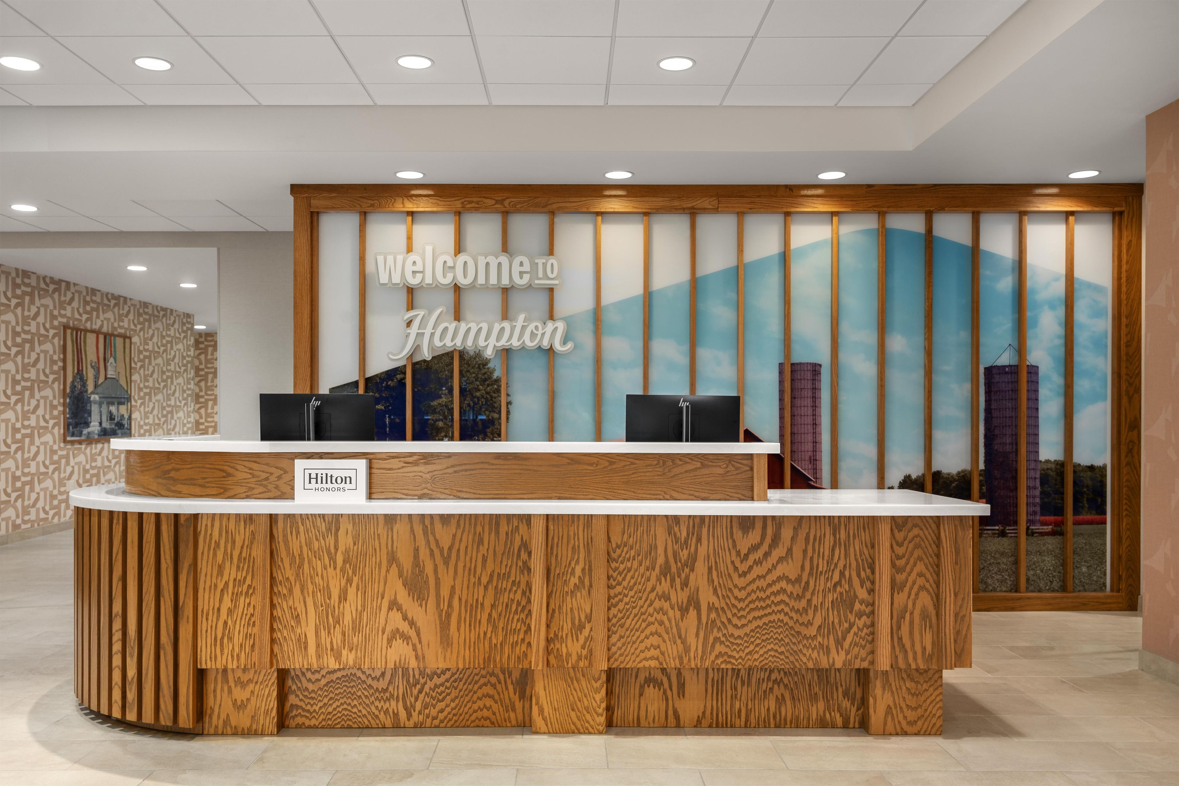 En receptionsdisk med et 'Welcome to Hampton' skilt, et fjernsyn og et 'Hilton Honors' skilt.