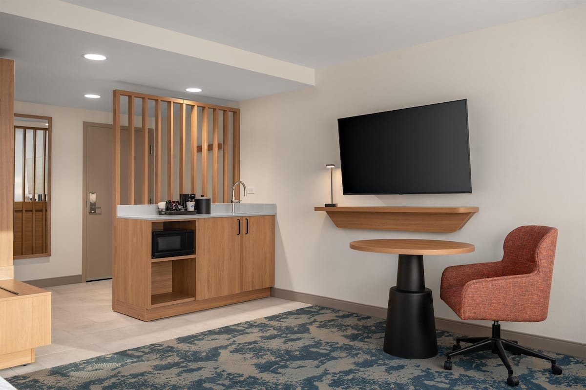Una habitación de hotel moderna con un armario de madera, un televisor de pantalla plana, una mesa redonda y una silla roja.