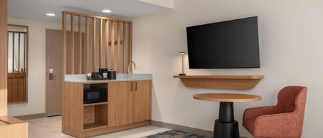 Una habitación de hotel moderna con un armario de madera, un televisor de pantalla plana, una mesa redonda y una silla roja.