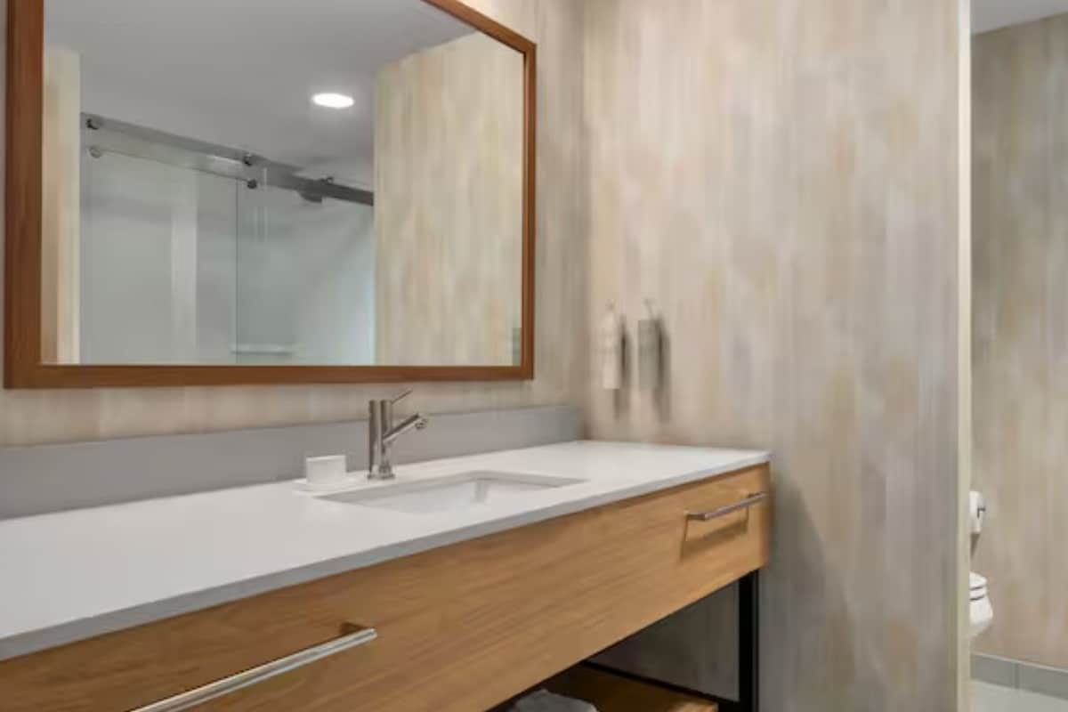 A modern bathroom with a white sink, wooden vanity, and a large mirror.