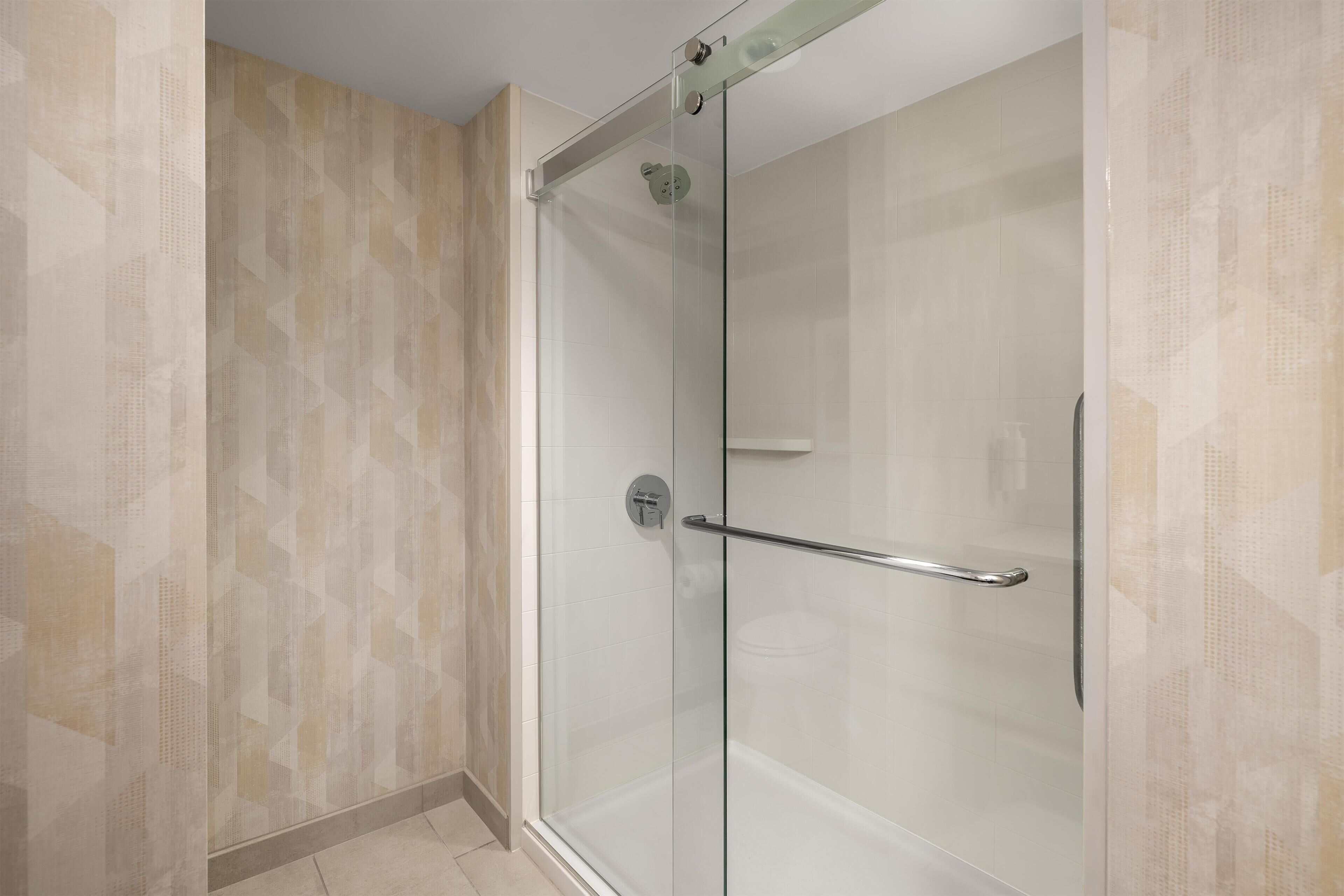 A glass-enclosed shower with a handrail, tiled walls, and a patterned wall design.