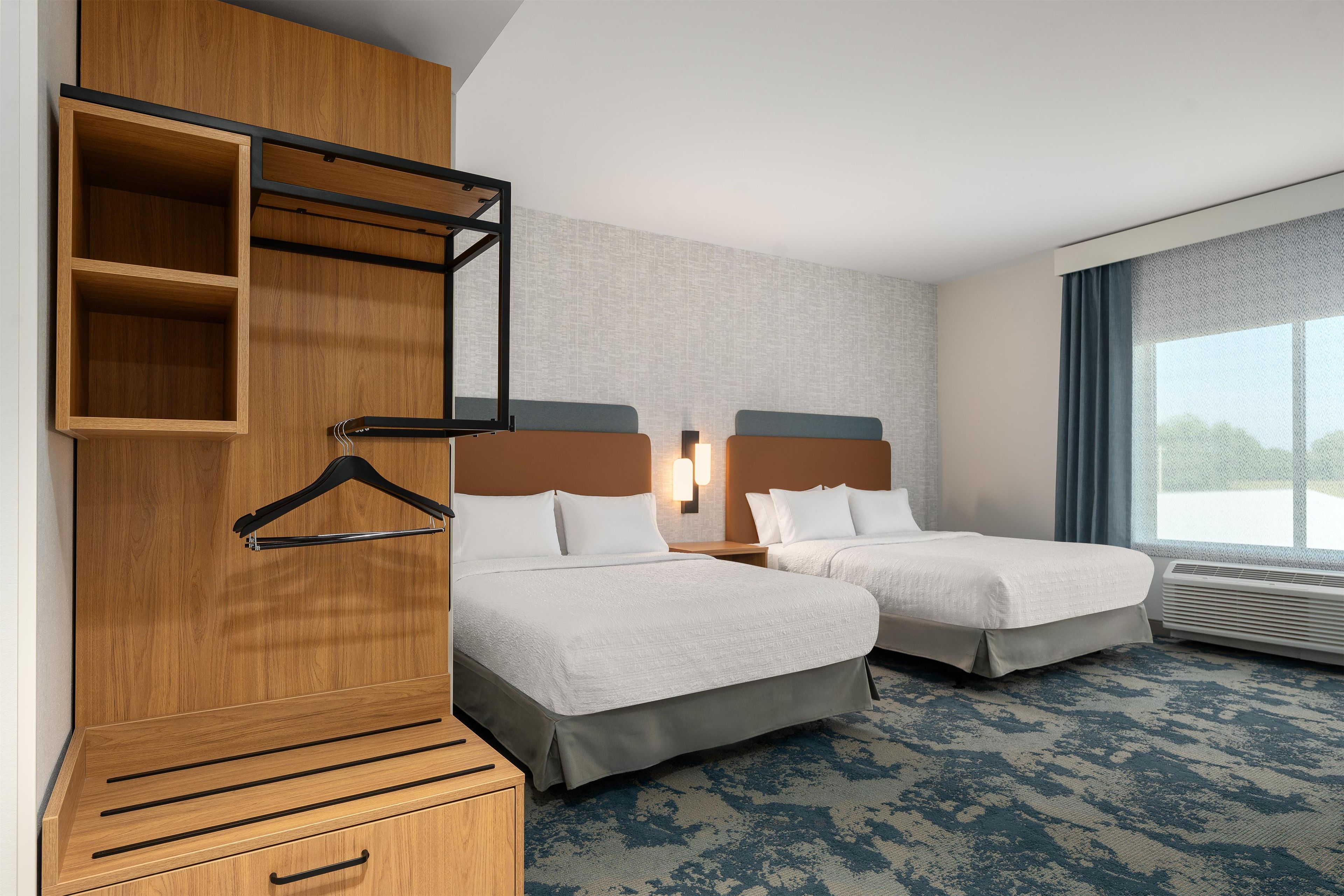 Ein Hotelzimmer mit zwei Betten, einem Holzschrank, einer Kleiderstange und einem großen Fenster mit Blick.