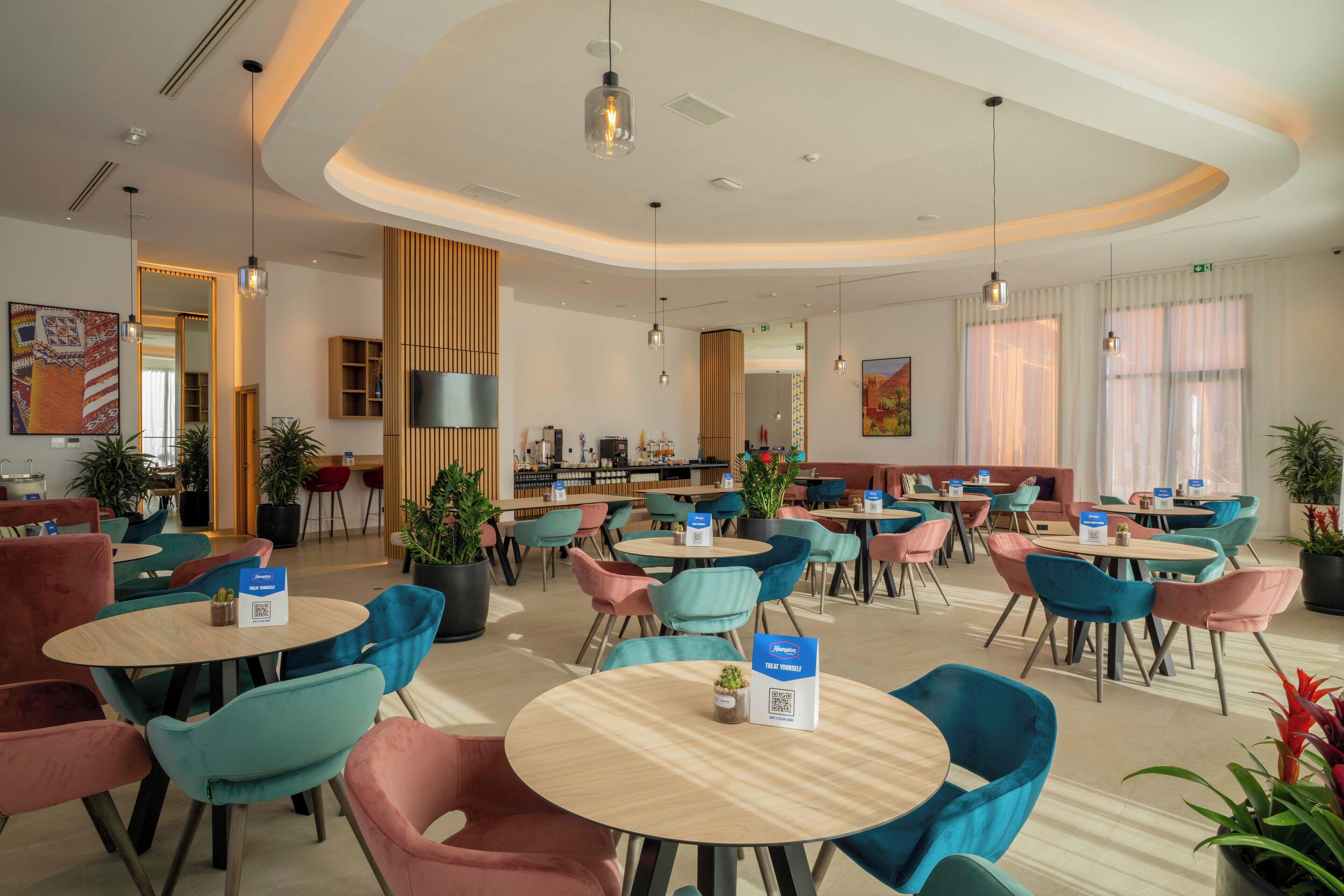 A modern hotel lobby with round tables, colorful chairs, and potted plants.