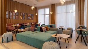A modern lounge area with seating arrangements, including sofas and chairs, and a wall adorned with framed artwork. - Hampton By Hilton Ben Guerir (Ben Guerir)