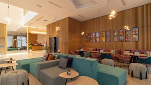 A modern lounge area with teal and grey seating, wooden panel walls, and pendant lighting. - Hampton By Hilton Ben Guerir (Ben Guerir)