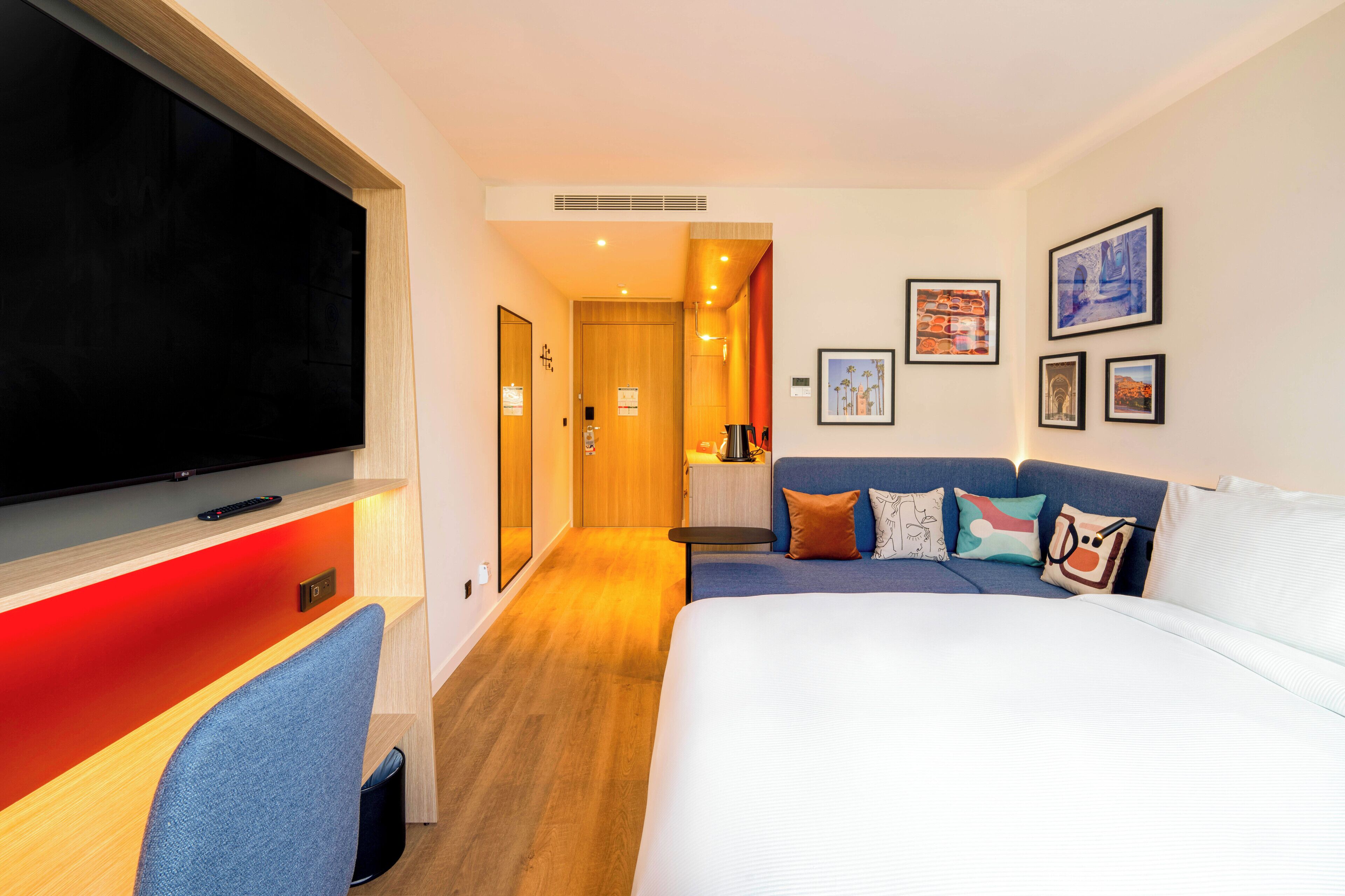 A hotel room with a large bed, a TV, a desk with a chair, and a sofa.