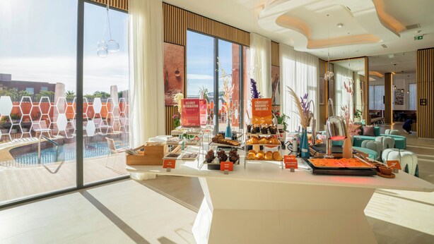 A hotel lobby with a pool view, a reception desk, and various amenities. - Hampton By Hilton Ben Guerir (Ben Guerir)