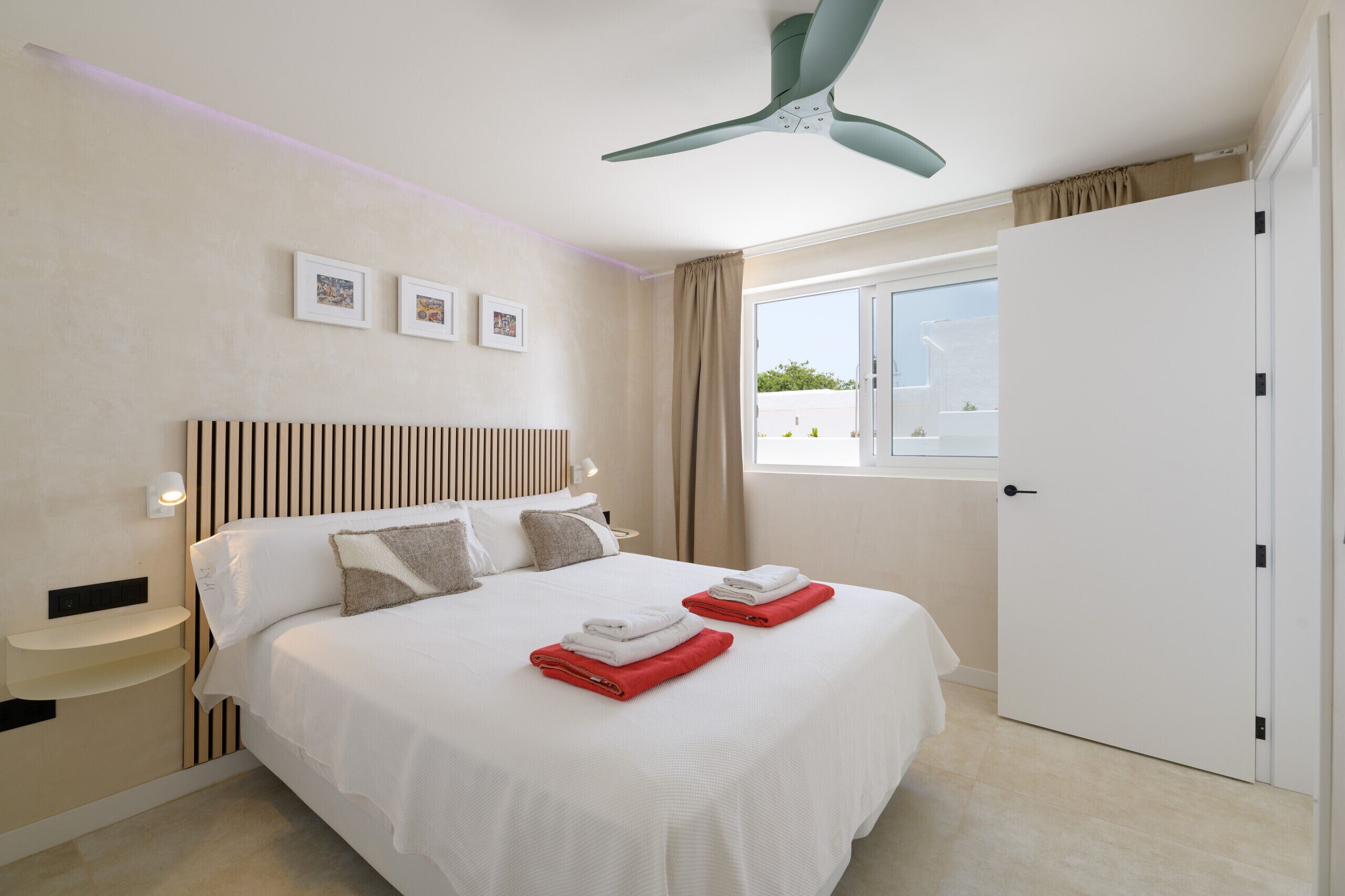 Una habitación de hotel con cama, ventilador de techo, ventana con cortinas y puerta.