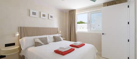 Una habitación de hotel con cama, ventilador de techo, ventana con cortinas y puerta.