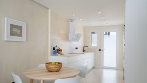 A modern kitchen with white cabinets, a dining table with chairs, and a basket of apples on the table. - Casa Xabi, Private terrace - Puerto del Carmen (Puerto del Carmen)