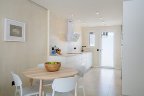 A modern kitchen with white cabinets, a dining table with chairs, and a basket of apples on the table. - Casa Xabi, Private terrace - Puerto del Carmen (Puerto del Carmen)
