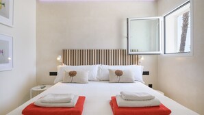 A hotel room with a bed, two pillows, a nightstand, a lamp, and a window with a view of palm trees. - Casa Xabi, Private terrace - Puerto del Carmen (Puerto del Carmen)