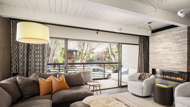 Una sala de estar moderna con un sofá modular, sillones, chimenea y ventanas amplias que ofrecen vistas al exterior.