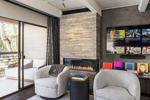 Ein modernes Wohnzimmer mit Kamin, bequemen Sitzmöglichkeiten und einem Flachbildfernseher, der eine Musik-Playlist anzeigt.