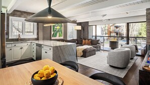 Una cocina moderna con armarios blancos, una isla de mármol y un comedor con mesa y sillas de madera.