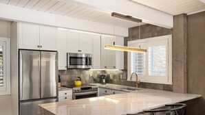 Una cocina moderna con electrodomésticos de acero inoxidable, una isla de mármol y sillas negras.