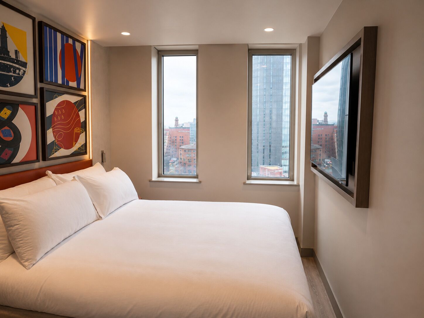 Una habitación de hotel con una cama grande, dos ventanas y obras de arte en las paredes.