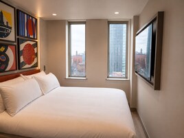 Una habitación de hotel con una cama grande, dos ventanas y obras de arte en las paredes.