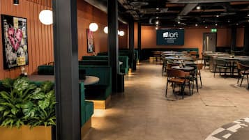 Un restaurante moderno con asientos tipo banqueta verdes y mesas redondas, una pantalla grande que muestra el logotipo y una pared con una obra de arte con forma de corazón.
