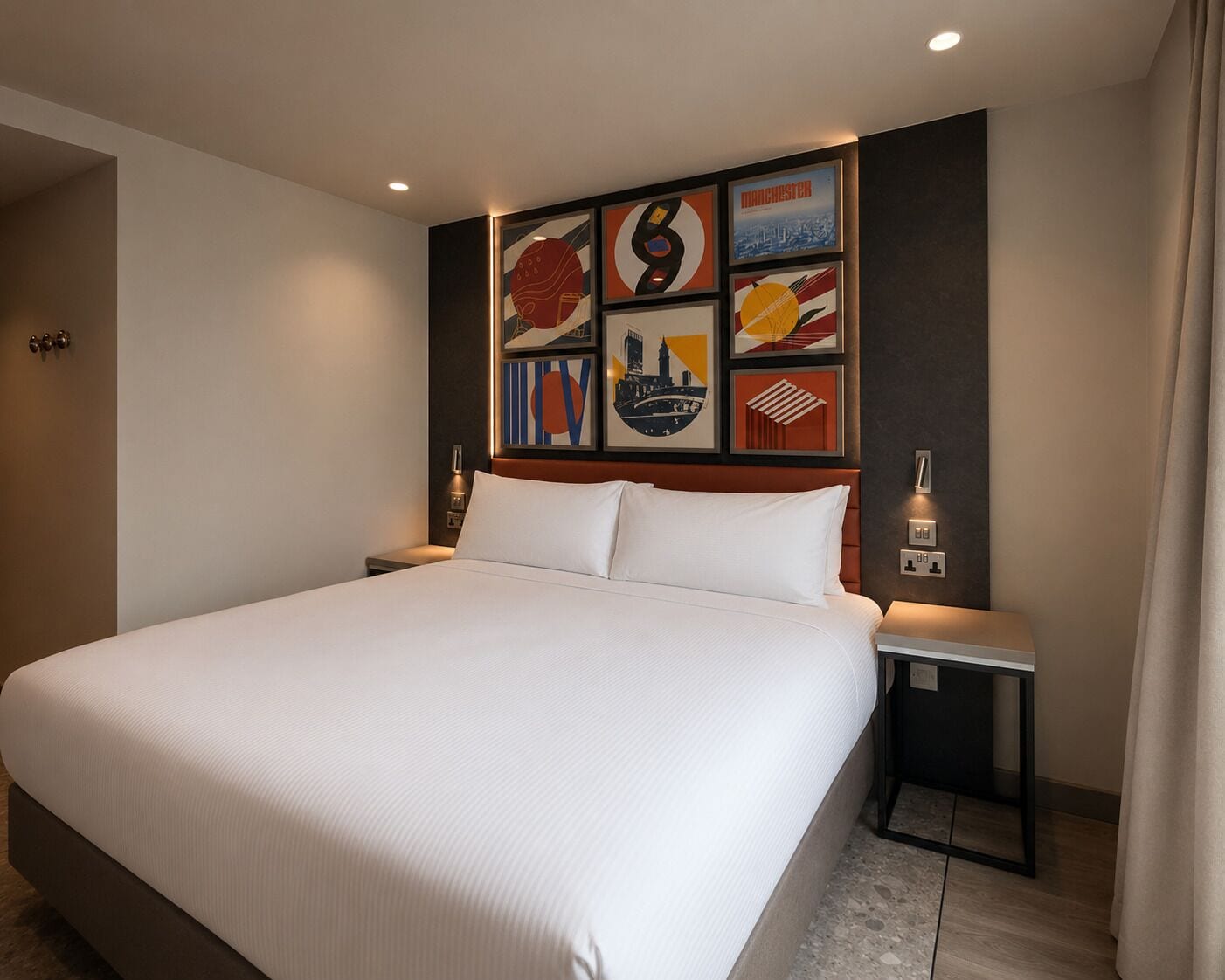 A hotel room with a large bed, a headboard with artwork, bedside tables, and a door.