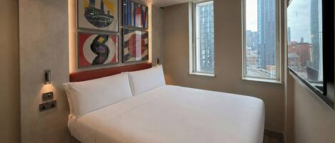 A hotel room with a large bed, multiple windows, and artwork on the wall.