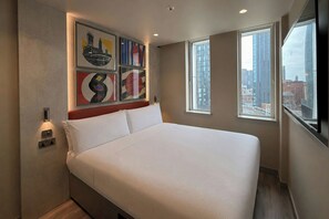 Habitación de hotel con una cama grande, varias ventanas y cuadros en la pared.