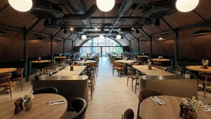 Un restaurante amplio con techos altos, mesas redondas e iluminación colgante.
