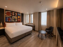 Habitación de hotel con una cama grande, un escritorio, dos sillas y una pared con arte abstracto.
