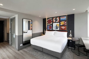 Habitación de hotel moderna con una cama grande, un escritorio y una silla. Se aprecia una pared con cuadros enmarcados y un espejo.