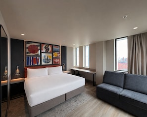 Una habitación de hotel moderna con una cama grande, un sofá, un escritorio y obras de arte en la pared.