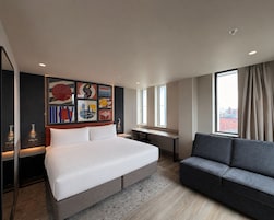 Una habitación de hotel moderna con una cama grande, un sofá, un escritorio y obras de arte en la pared.