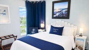 Ein ordentlich eingerichtetes Schlafzimmer mit einem Bett, zwei Nachttischen, einem Fenster mit Vorhängen und einem gerahmten Bild an der Wand.