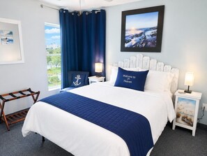 Une chambre à coucher bien rangée, avec un lit, deux tables de chevet, une commode, une fenêtre avec des rideaux et un tableau encadré au mur.