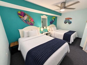 Une chambre d’hôtel avec deux lits, un ventilateur de plafond, un miroir et une décoration sur le thème du surf.