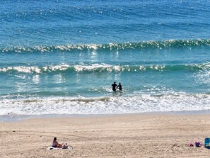 Ein Strand mit sandigem Ufer und einer Person, die auf einem Handtuch sitzt.