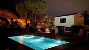 Een zwembad 's nachts met een modern huis op de achtergrond.