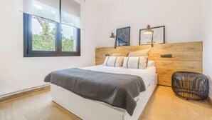 Een moderne slaapkamer met een groot bed, een houten hoofdbord, twee ingelijste kaarten en een rond rieten pouf.