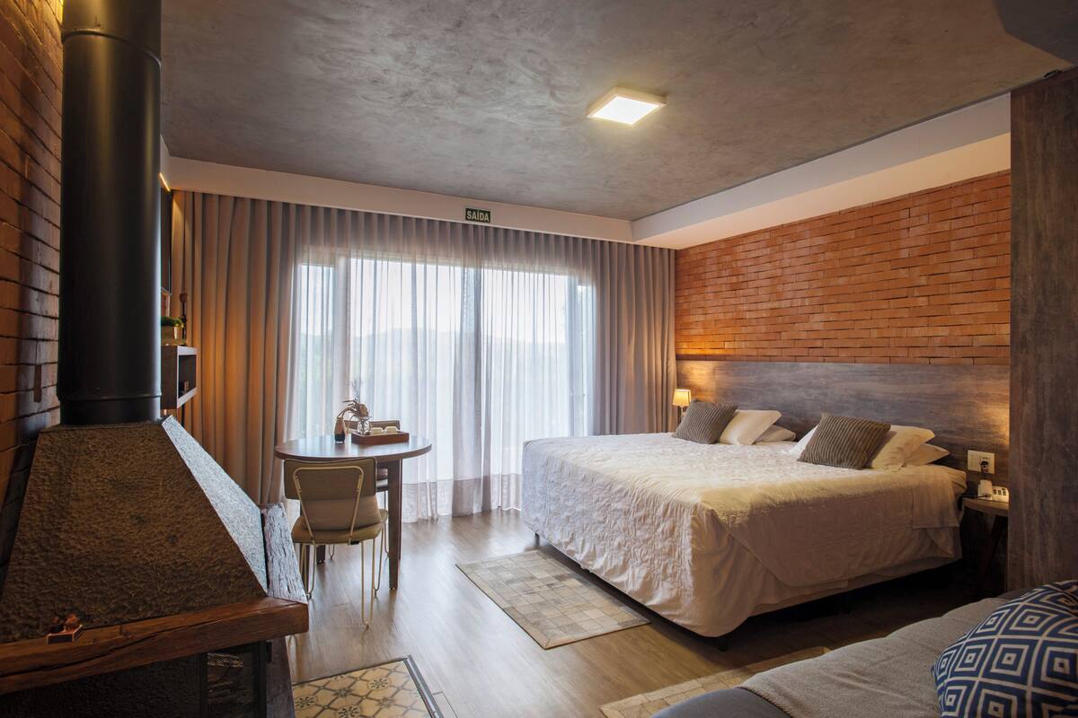 Ein Hotelzimmer mit Bett, einem kleinen Tisch, einem Sessel, einem Kamin und einer Backsteinwand.