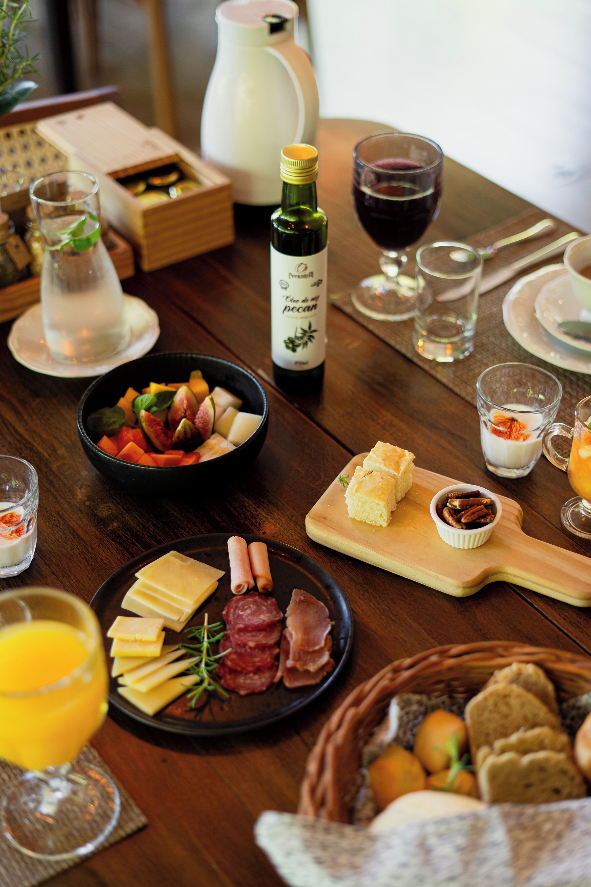 Une table en bois sur laquelle sont disposés divers aliments, notamment du fromage, des fruits et du pain, ainsi que des verres de vin et de jus de fruits.